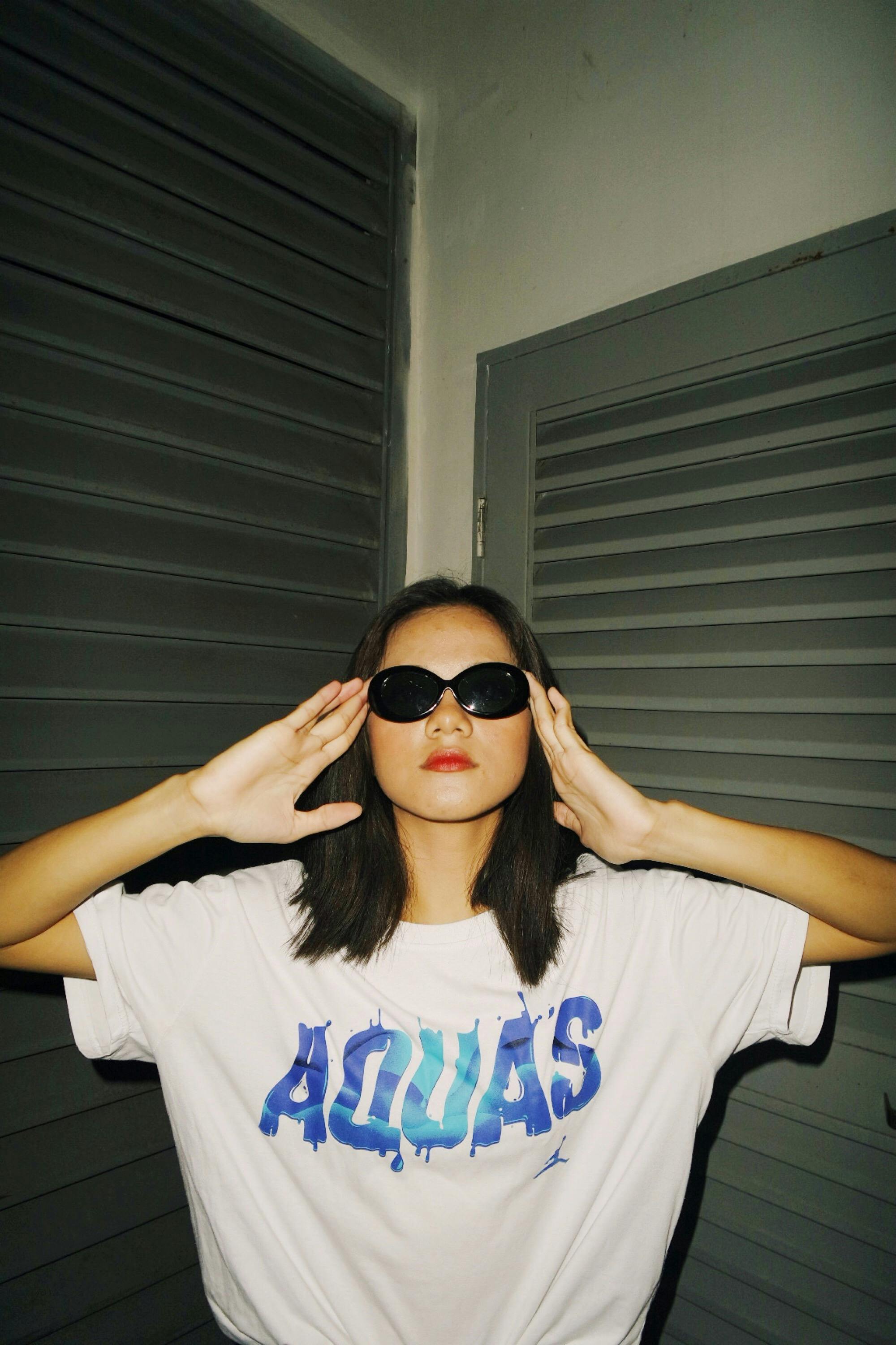 A woman in sunglasses and a graphic t-shirt poses for a flash photo