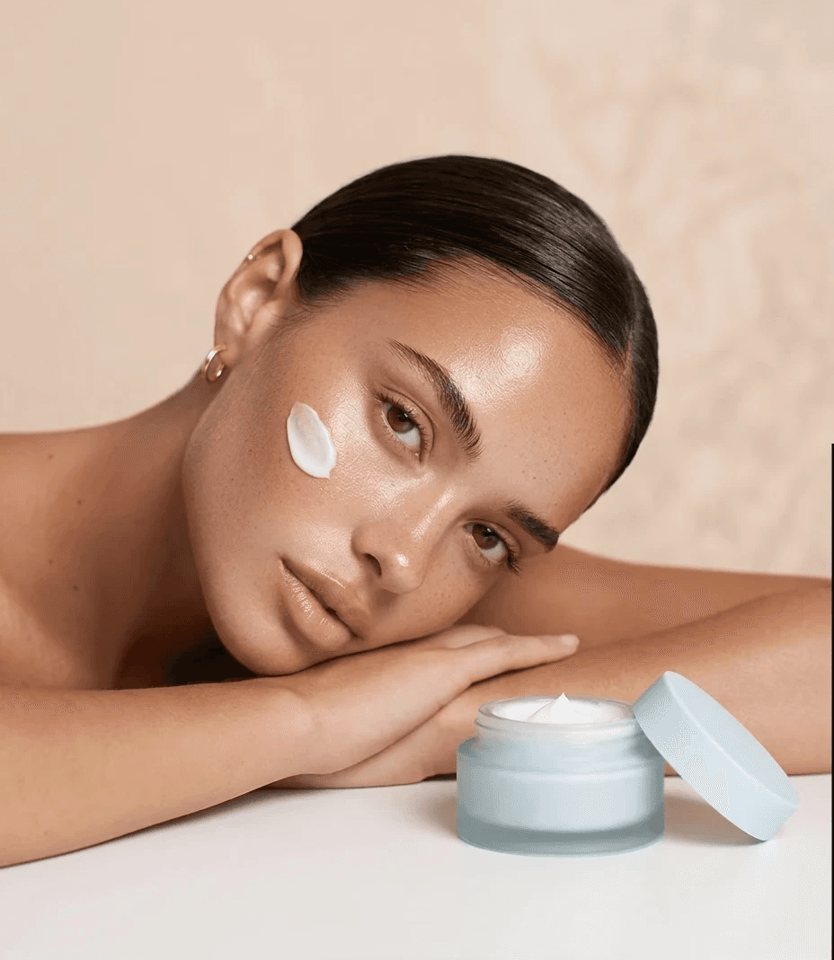 Model with face cream swatch next to open moisturizer jar