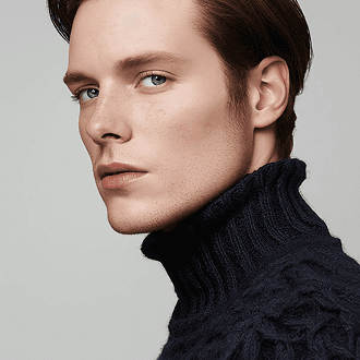 A man wearing a blue sweater stands, smiling at the camera.