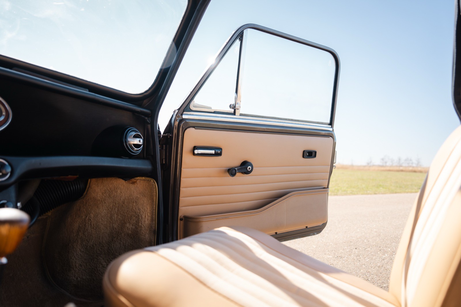 Interior view of a car door open to reveal a clear blue sky and sandy terrain outside.