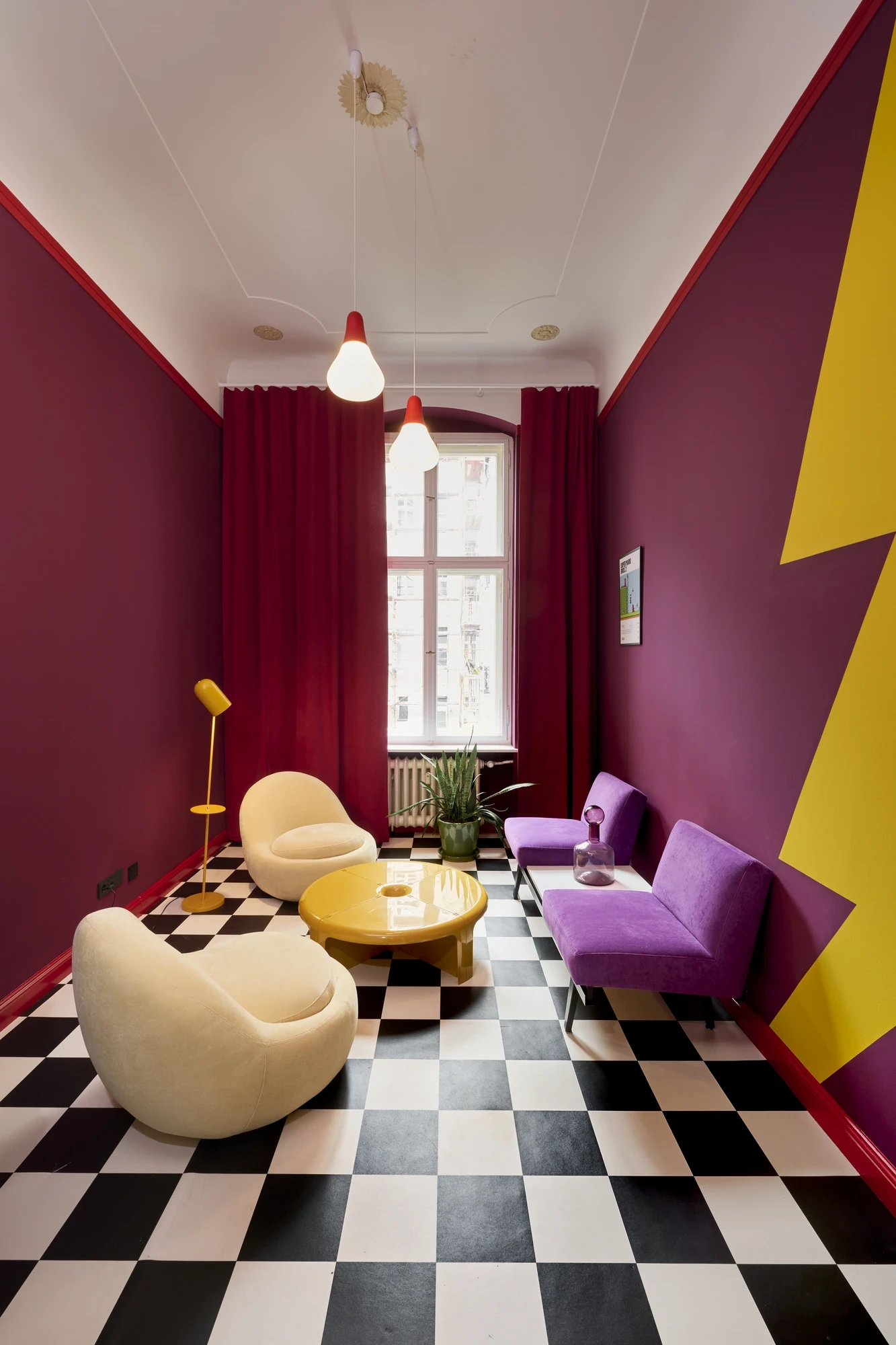 Lounge room with black-and-white checkerboard floor, burgundy walls, two cream pebble armchairs, a purple sofa and a yellow zig-zag graphic wall.