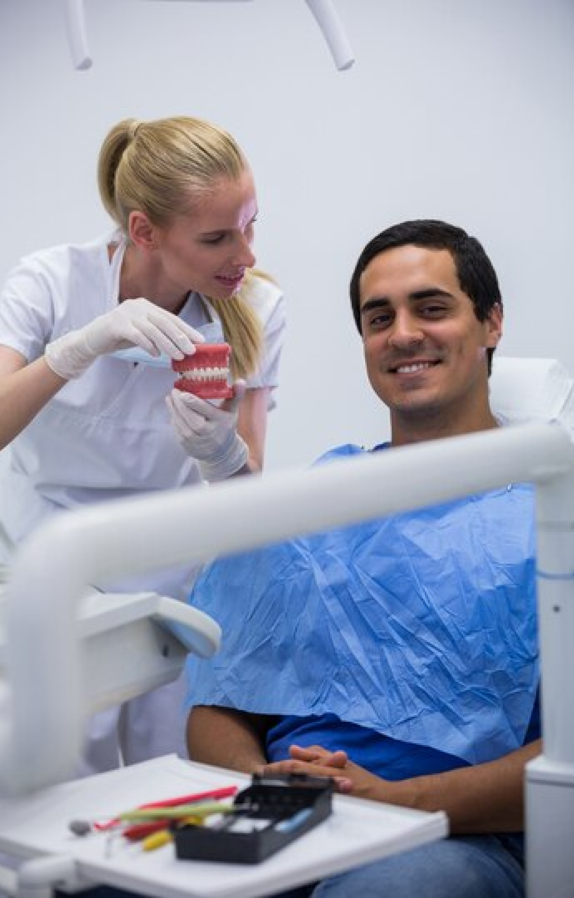 A dental professional showing a dental model to a smiling male patient sitting in a dental chair during a consultation.