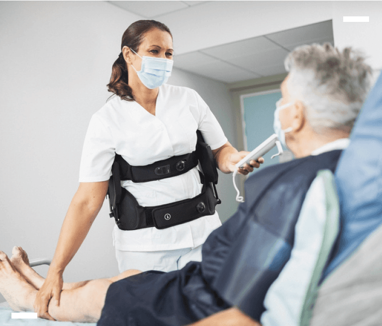 Healthcare professional wearing the Japet.W+ exoskeleton while caring for a patient, reducing back strain during handling tasks.