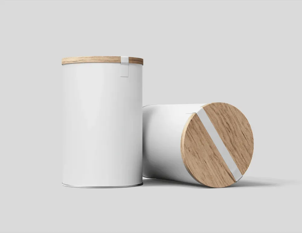 Two cylindrical packaging mockups with white bodies and wooden lids, one upright and one lying flat. Both feature an orange ribbon accent and are displayed against a light gray background.