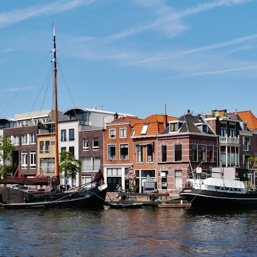 Canal with docked sailboats in front of a row of colorful buildings under a clear blue sky.