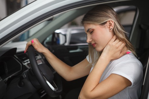 woman holding neck in pain one hand on the wheel