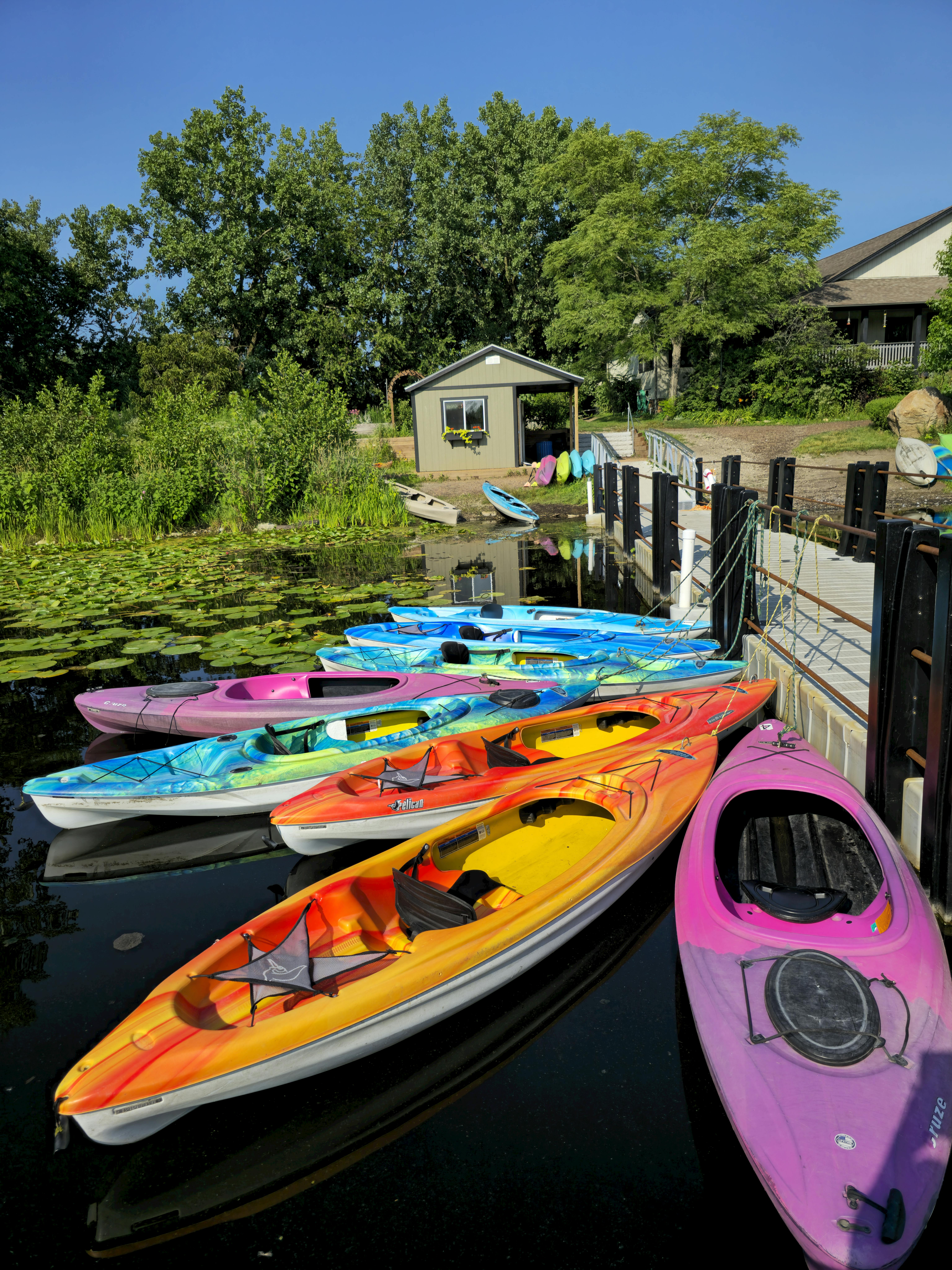 A young person with curly hair smiles at the camera while sitting in front of a laptop against a dark background.