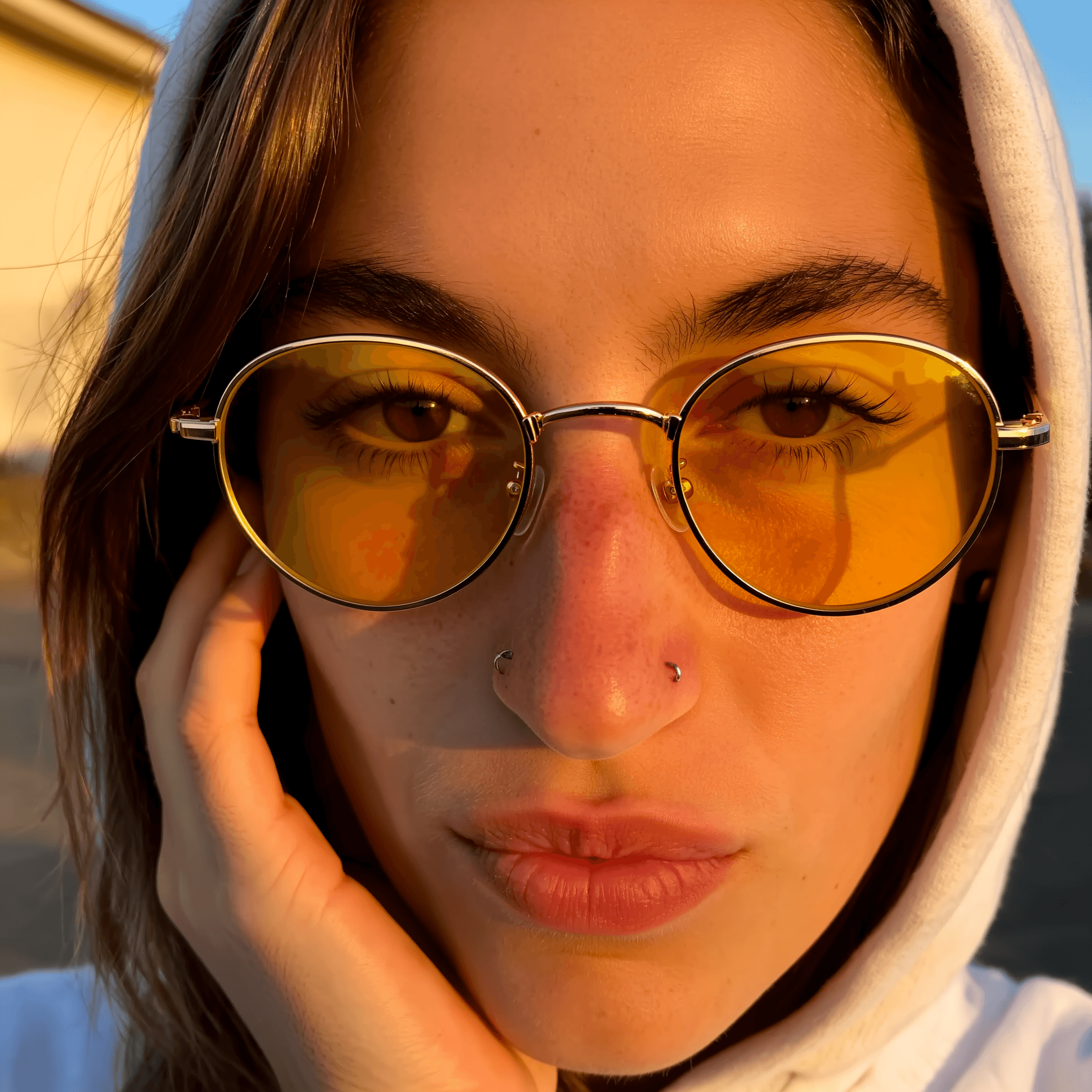 KI-Model in Nahaufnahme mit gelben Retro-Sonnenbrillen und Hoodie im warmen Abendlicht – modernes Porträt mit urbanem Look