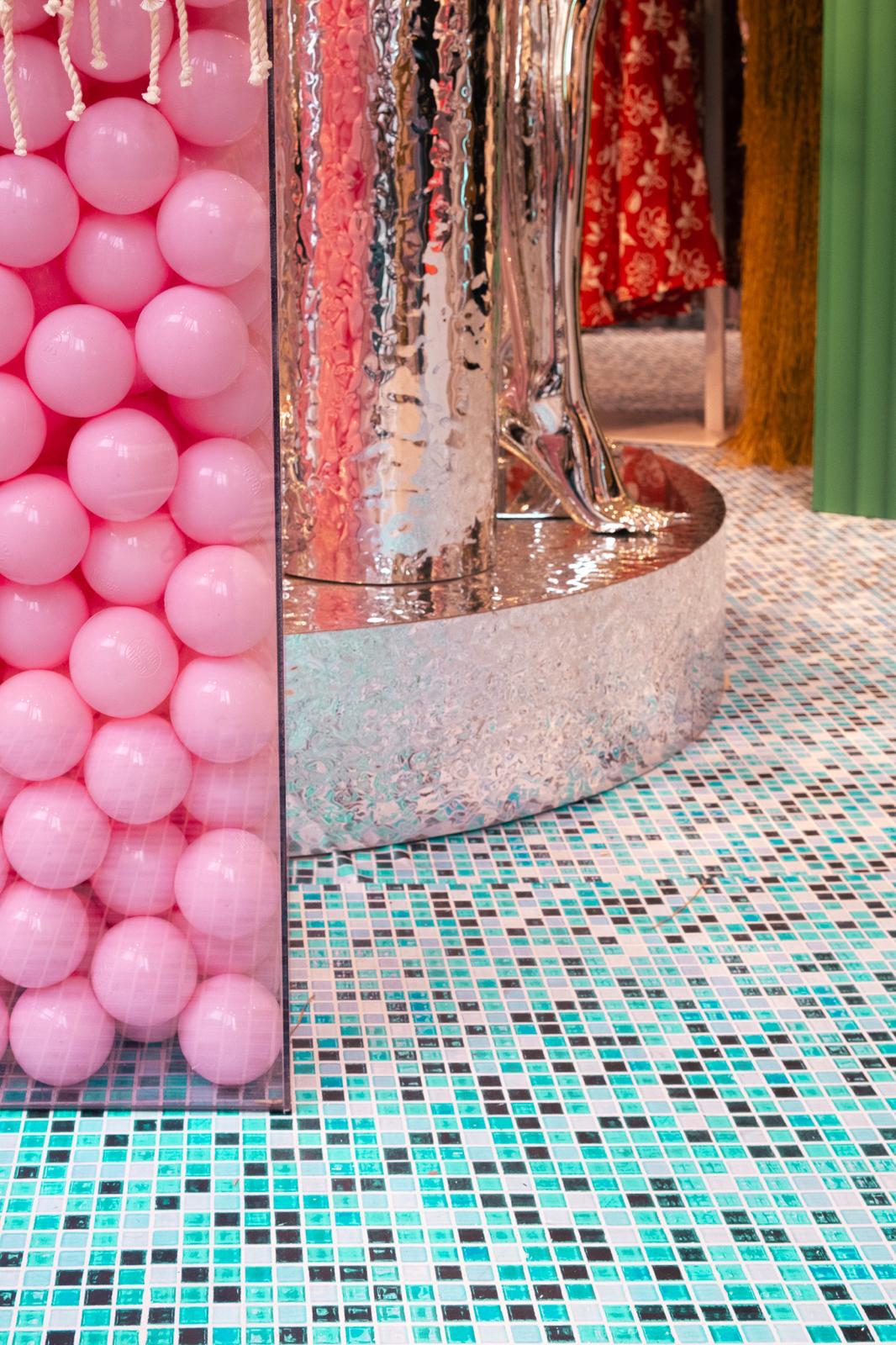Détail d'un socle métallique argenté et de boules de piscine roses sur un sol carrelé bleu turquoise.