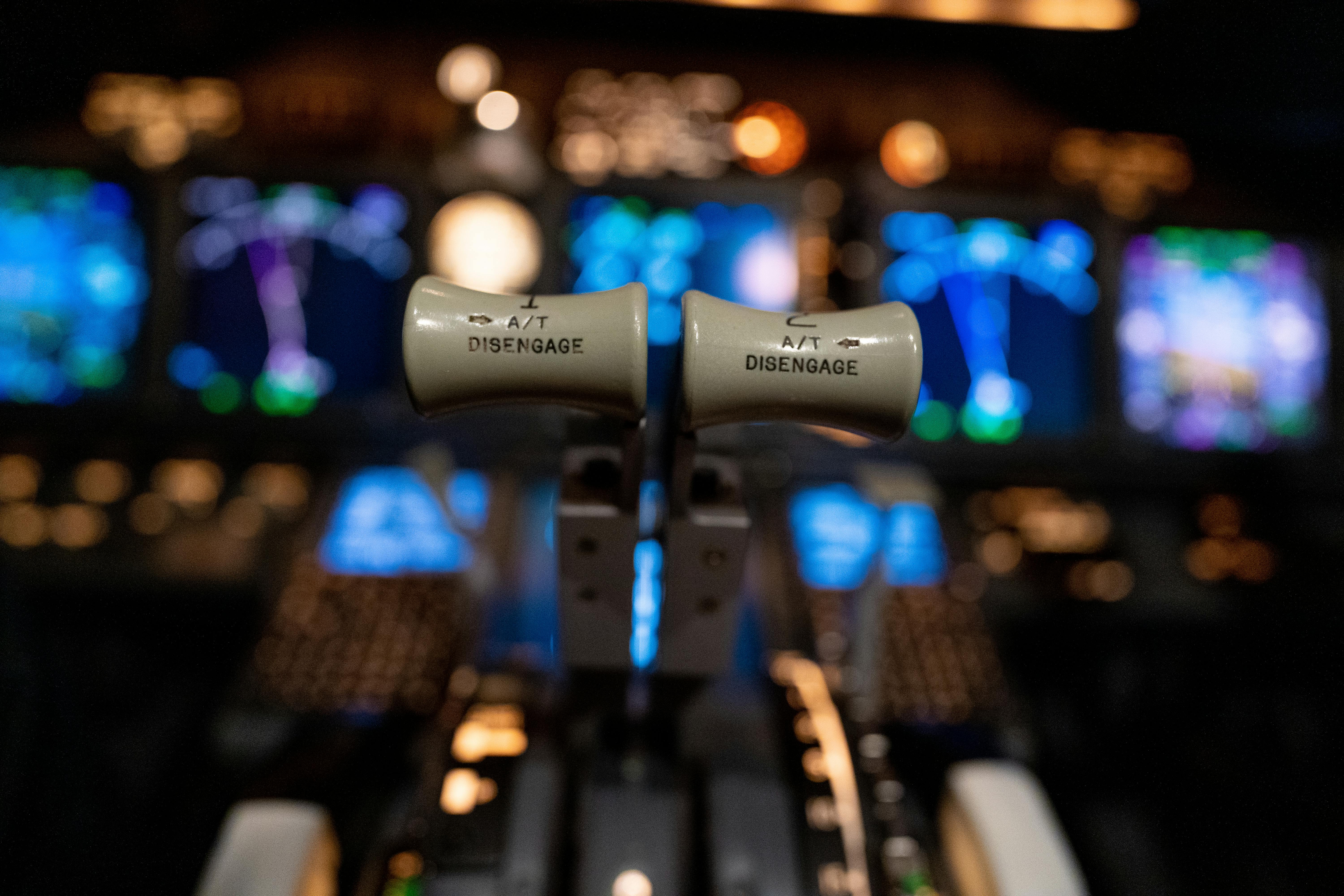 A young person with curly hair smiles at the camera while sitting in front of a laptop against a dark background.