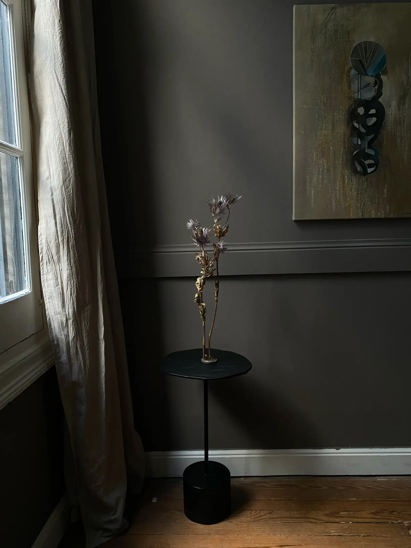 Fotografía minimalista de interior con flor seca dorada sobre mesa negra para proyectos de diseño que exploran el contraste entre luz y sombra.