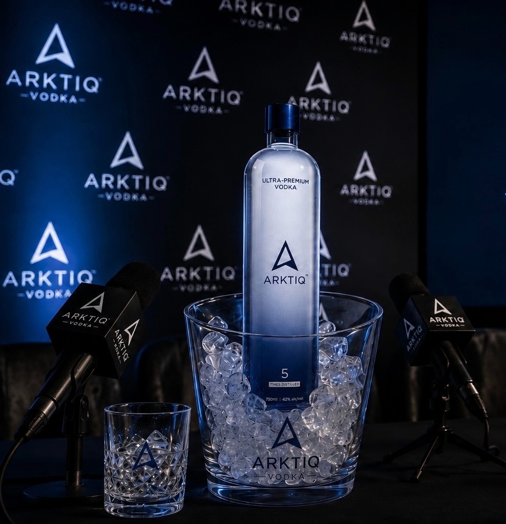 Arktiq Vodka bottle displayed on ice between microphones at a premium launch event.