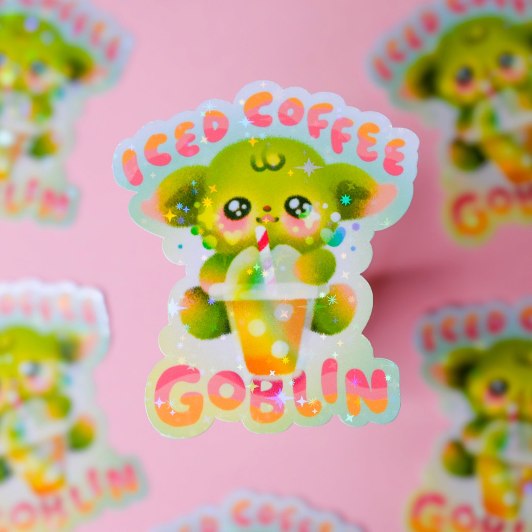 A sticker of a lime green goblin with a cup of iced coffee. It reads "Iced Coffee Goblin" in pink and orange text.