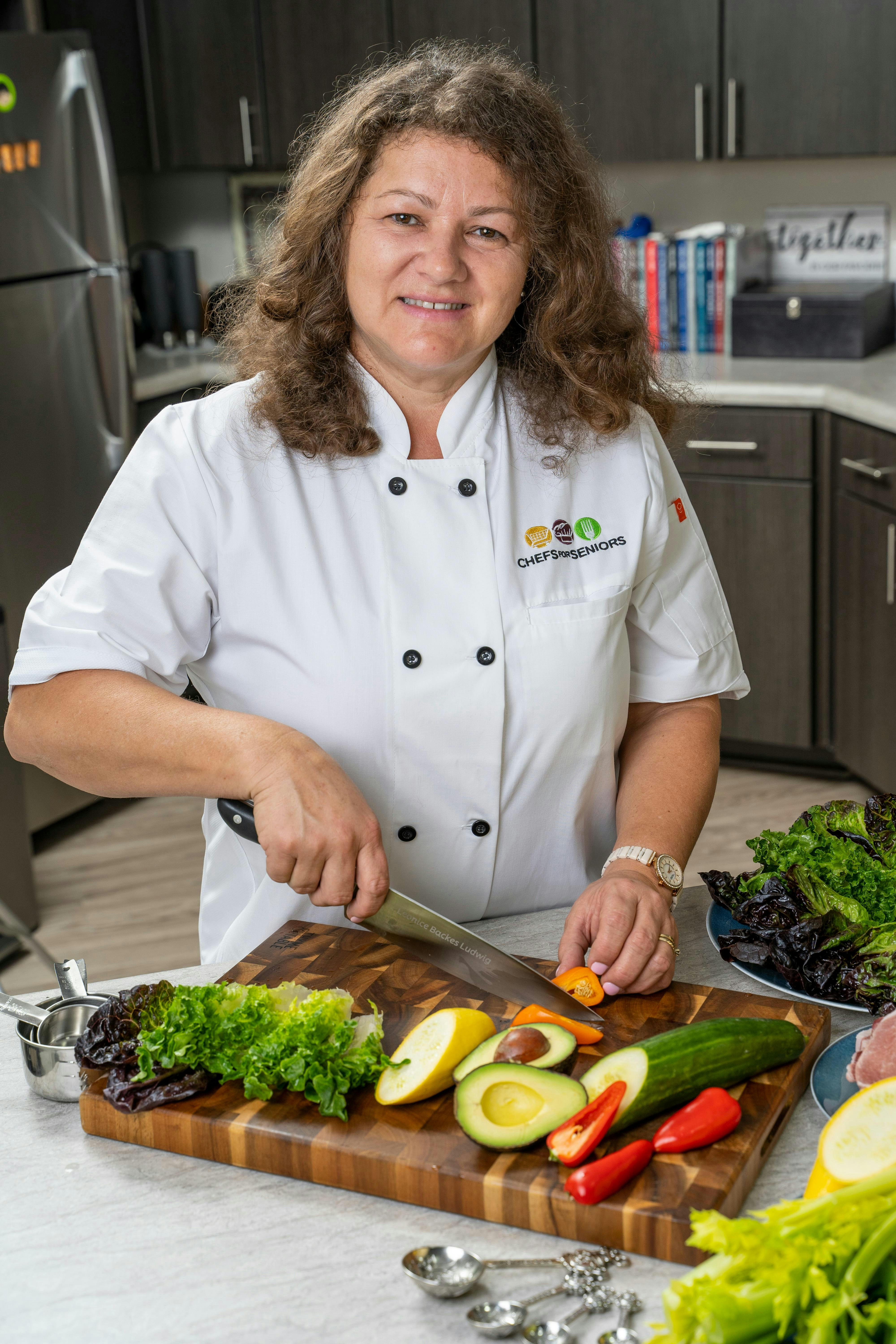 A woman in a chef's uniform cutting vegetables on a cutting board