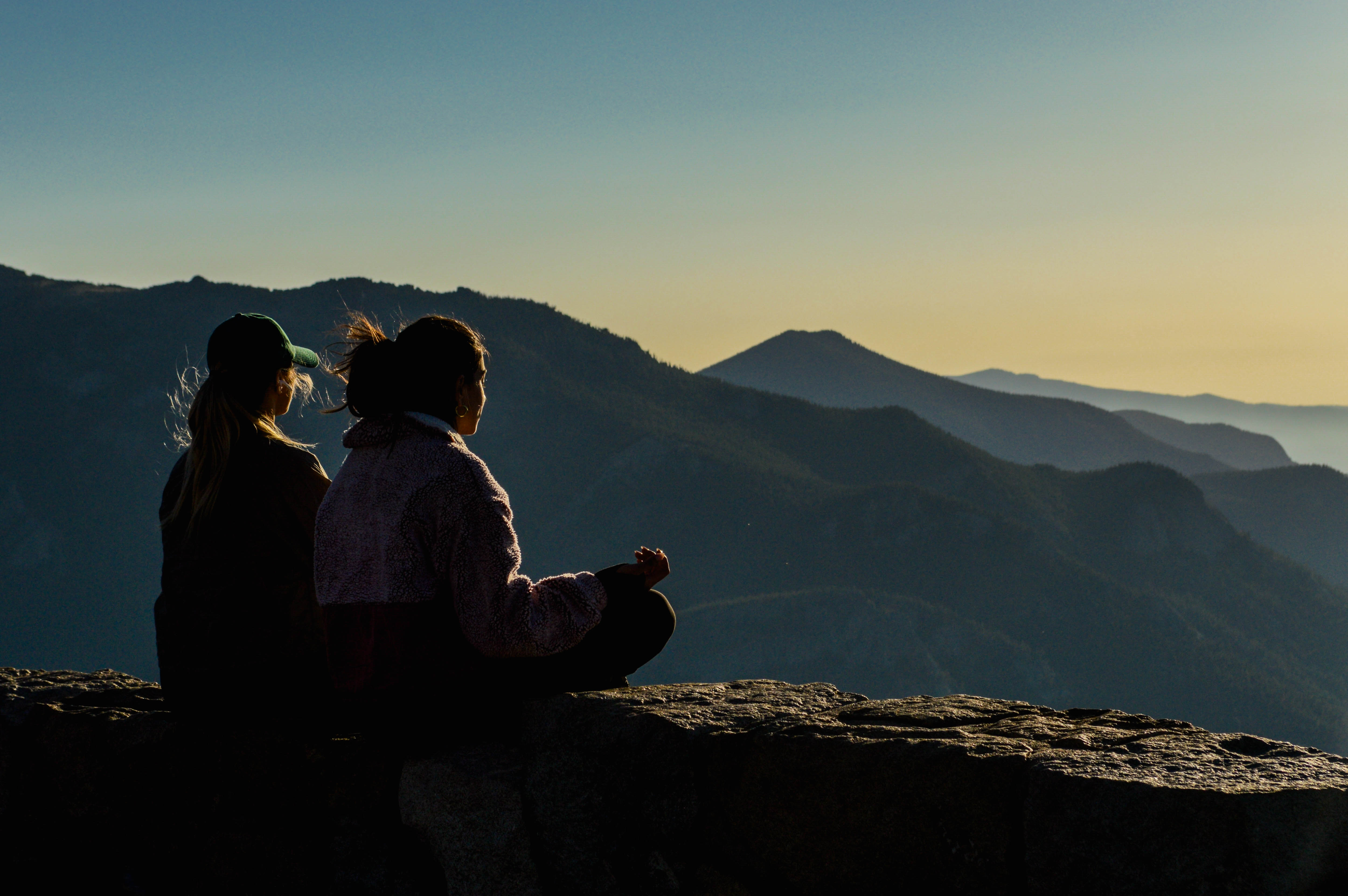 Two people sitting quietly overlooking mountains at sunset, practicing mindful breathing and reflection in nature.