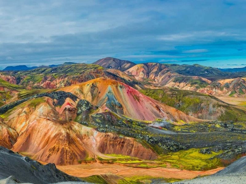 Colorful rhyolite mountains in Landmannalaugar, Iceland, displaying red, orange, yellow, and green hues formed by evolved lava, with rugged volcanic terrain stretching into the distance.