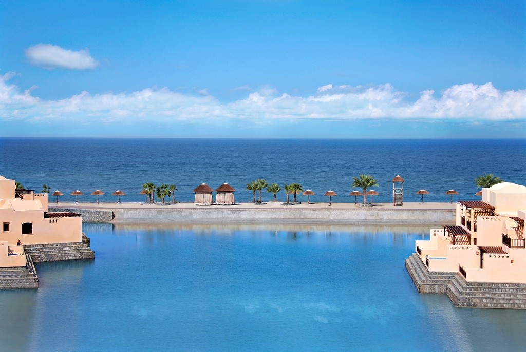 A bar with tables and chairs offers a scenic view of the ocean at Cove Rotana Resort.