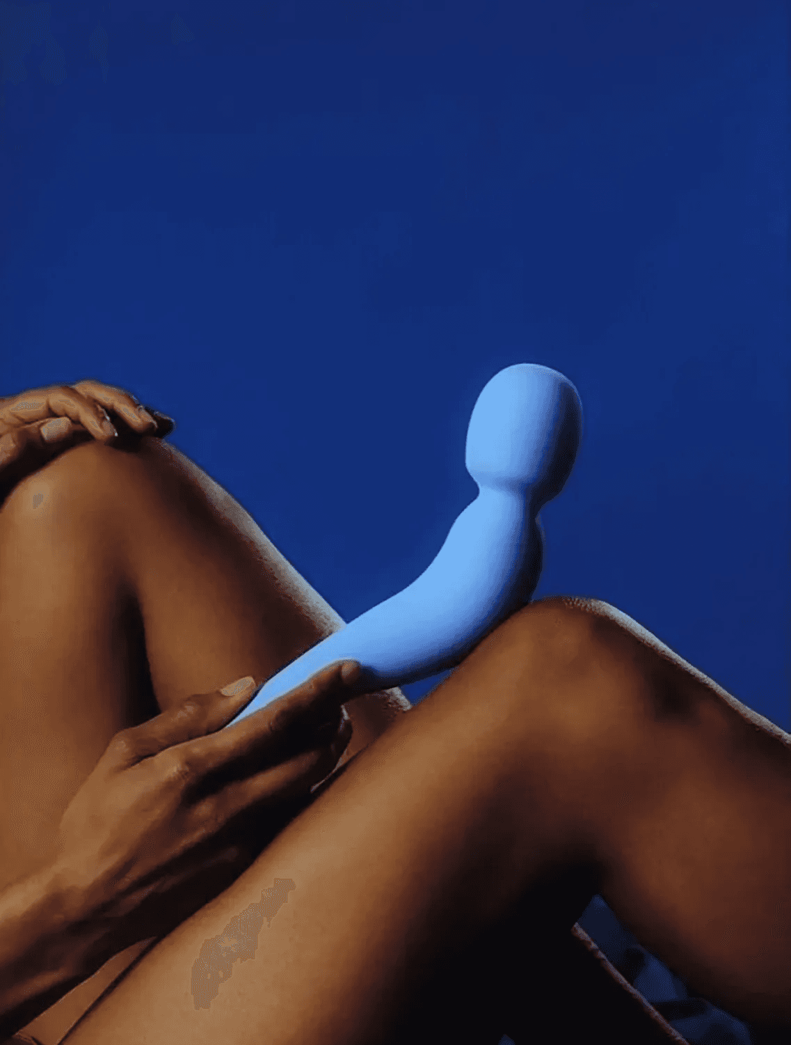 Person holding a blue Dame sexual wellness device against a deep blue background