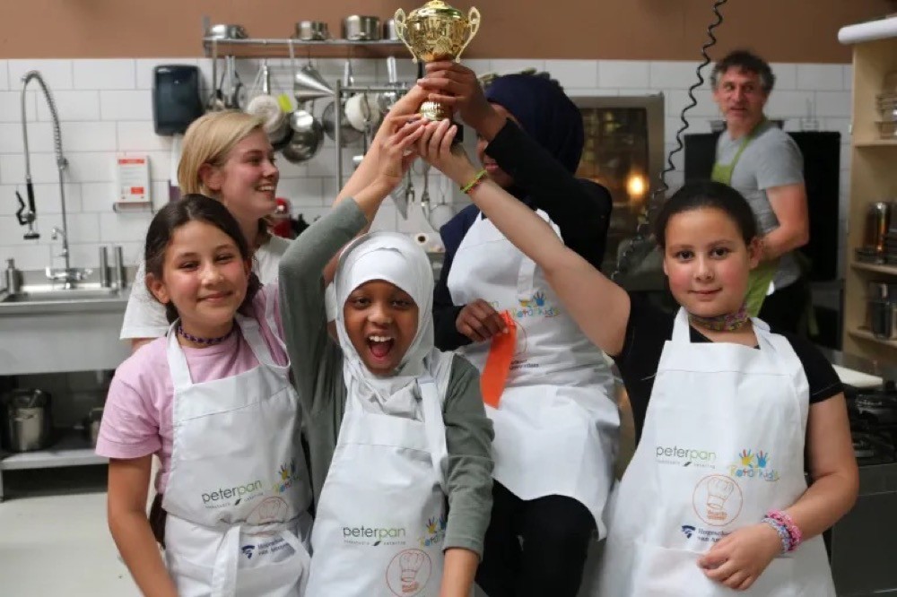 Kinderen houden samen een gouden beker omhoog in de keuken