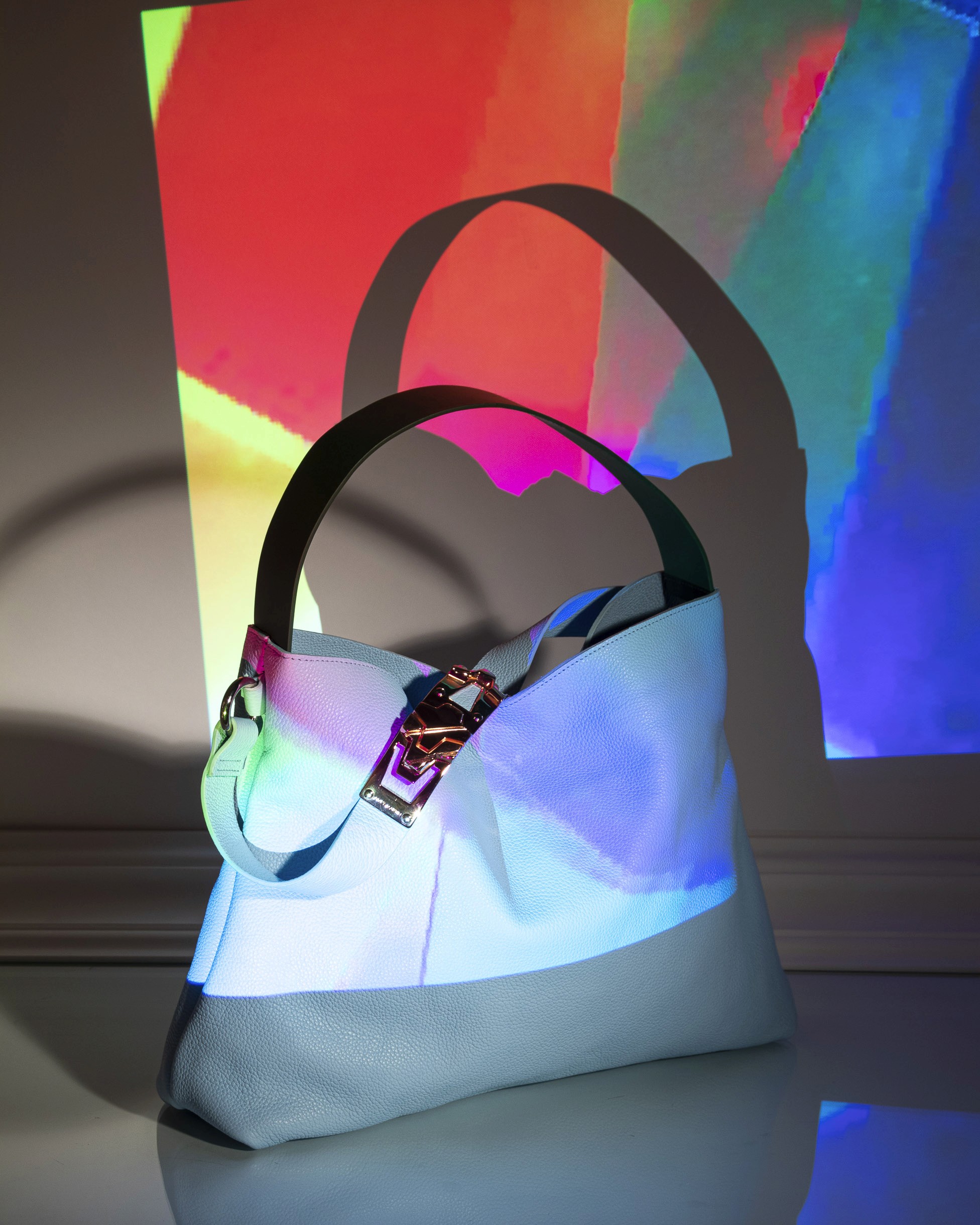 Photo conceptuelle d'un sac en cuir bleu ciel de la collection Amey Martin, éclairé par une image colorée diffusée par un projecteur orienté sur le sac