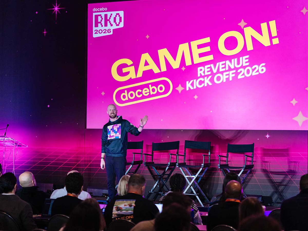 Presenter on stage at Docebo's Revenue Kick Off 2026, in front of a pink Game On event screen