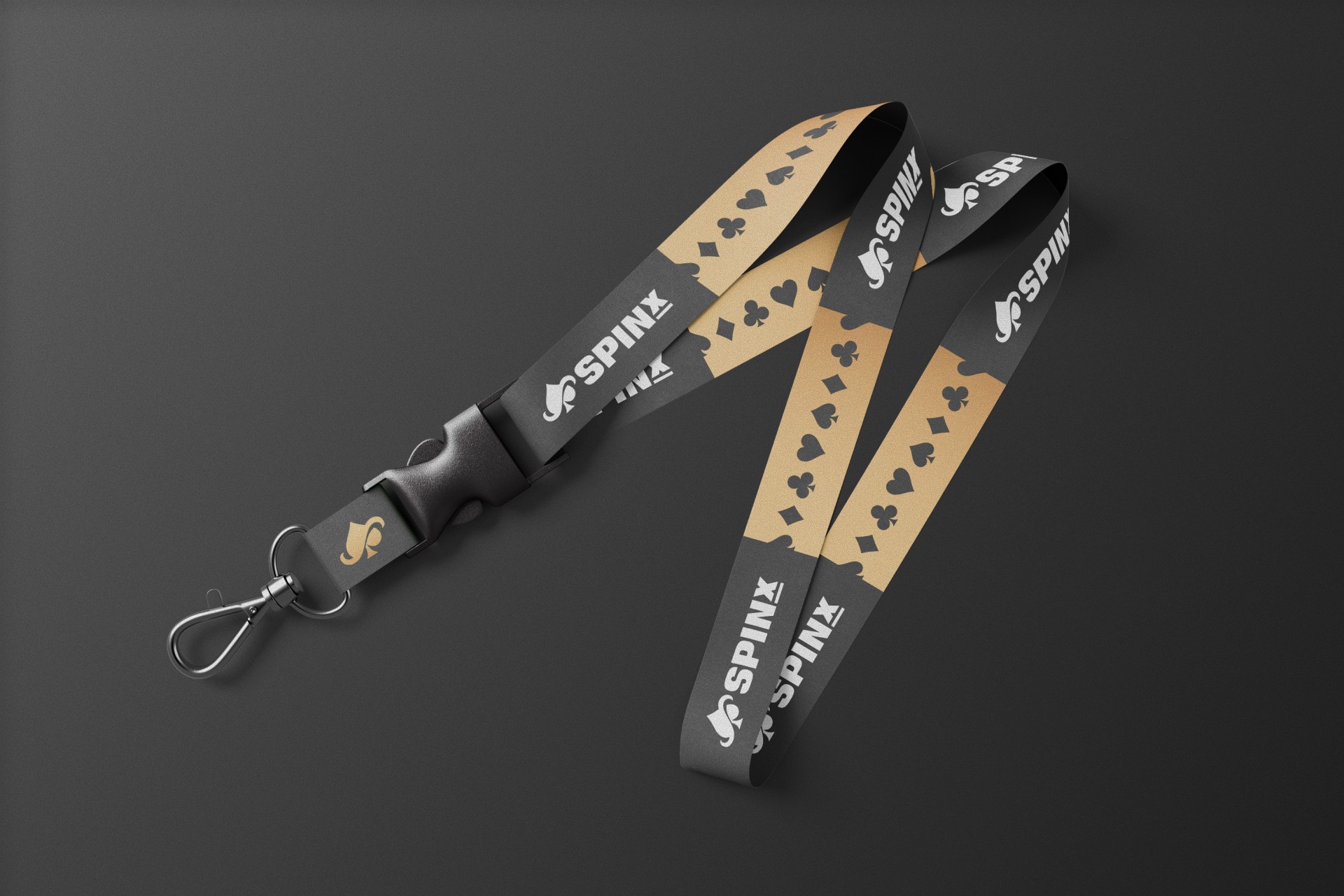 A black and beige lanyard on a dark surface features a repeating pattern of card suits and the "SpinX" logo in white. It has a metal clasp.