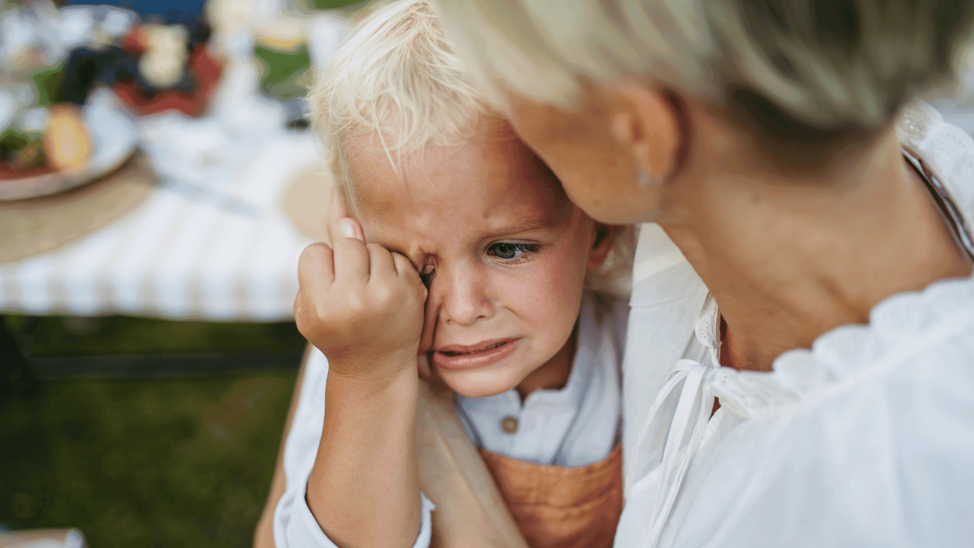 Alt text: A young child sitting on their mother’s lap, crying and looking stressed.
