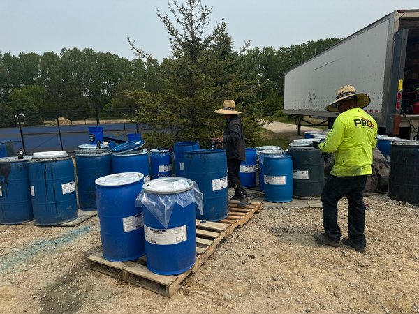 Crew members in sun hats beside blue drums on wooden pallets