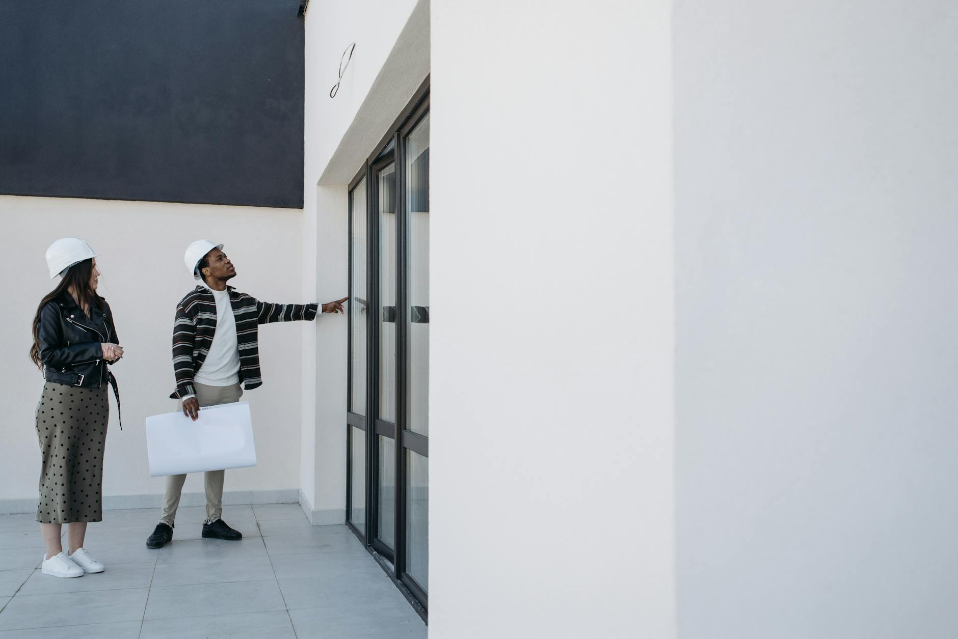 Two architects in hard hats examining the exterior of a modern white building with large windows