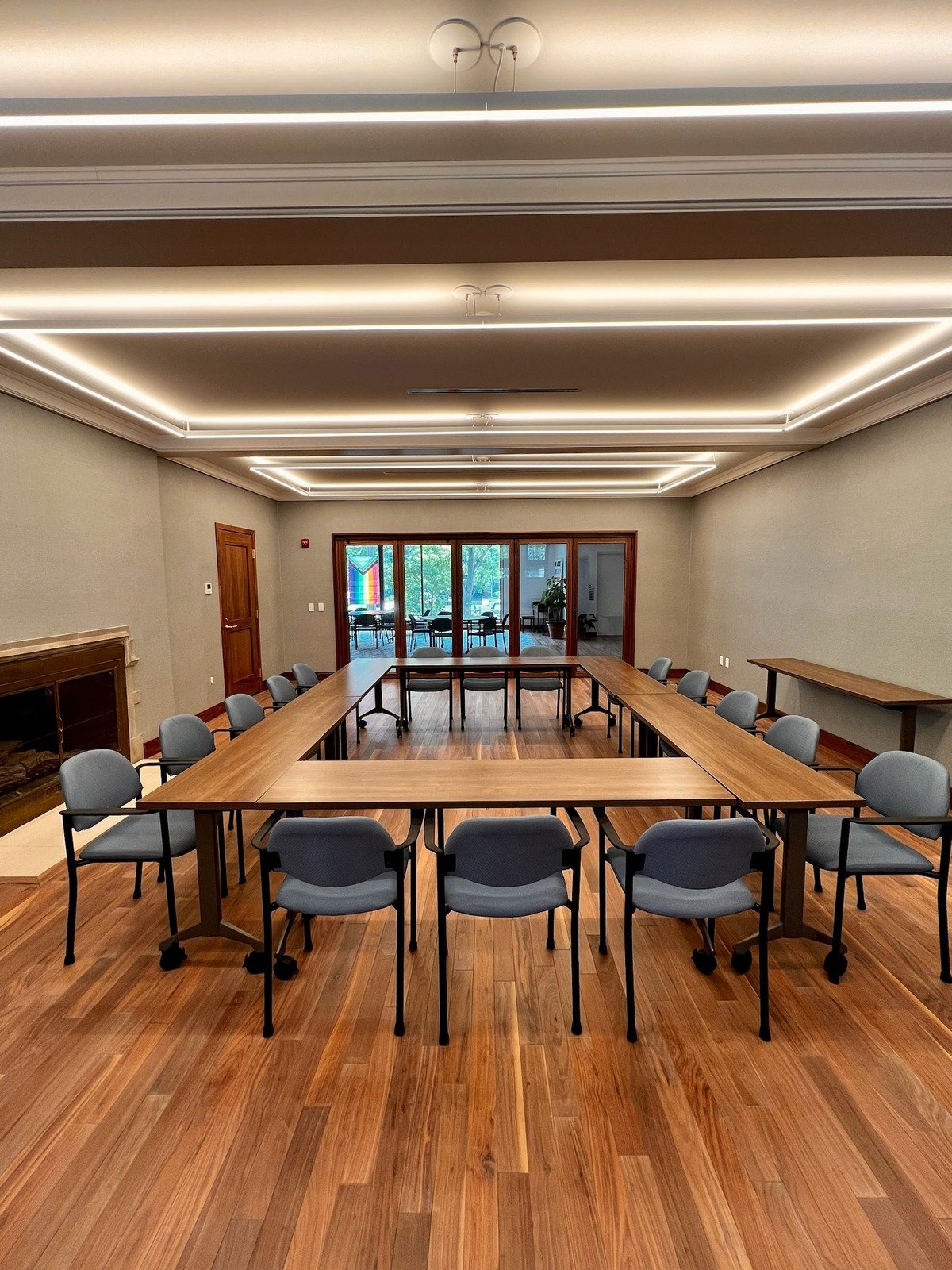 Gamble Room at Grace Trinity Church, set up with U-shaped tables and chairs, featuring a fireplace and large glass doors leading to a bright outdoor space.