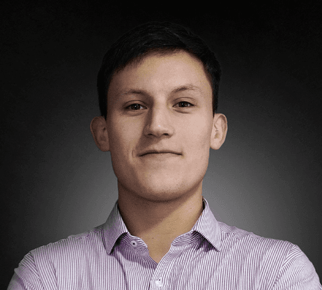 Woman with a short haircut smiling confidently, wearing a blazer and standing in warm natural light with modern architecture behind her.