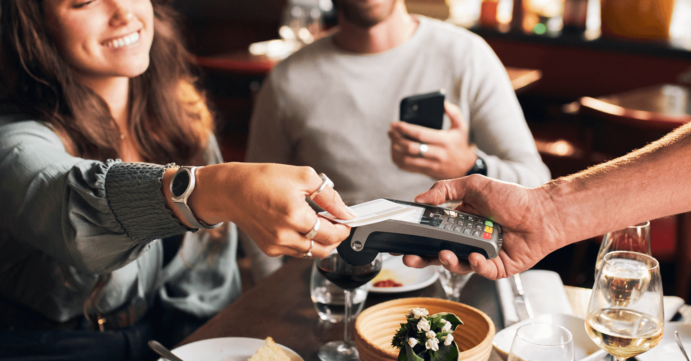 En kvinne smiler mens hun betaler for daten og mannen står i bakgrunnen og venter.