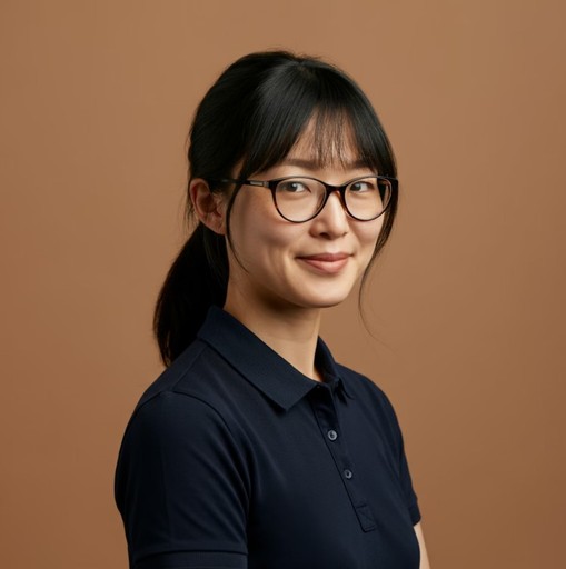 Person with glasses and dark hair tied back, wearing a navy shirt, posing in front of a plain brown background.