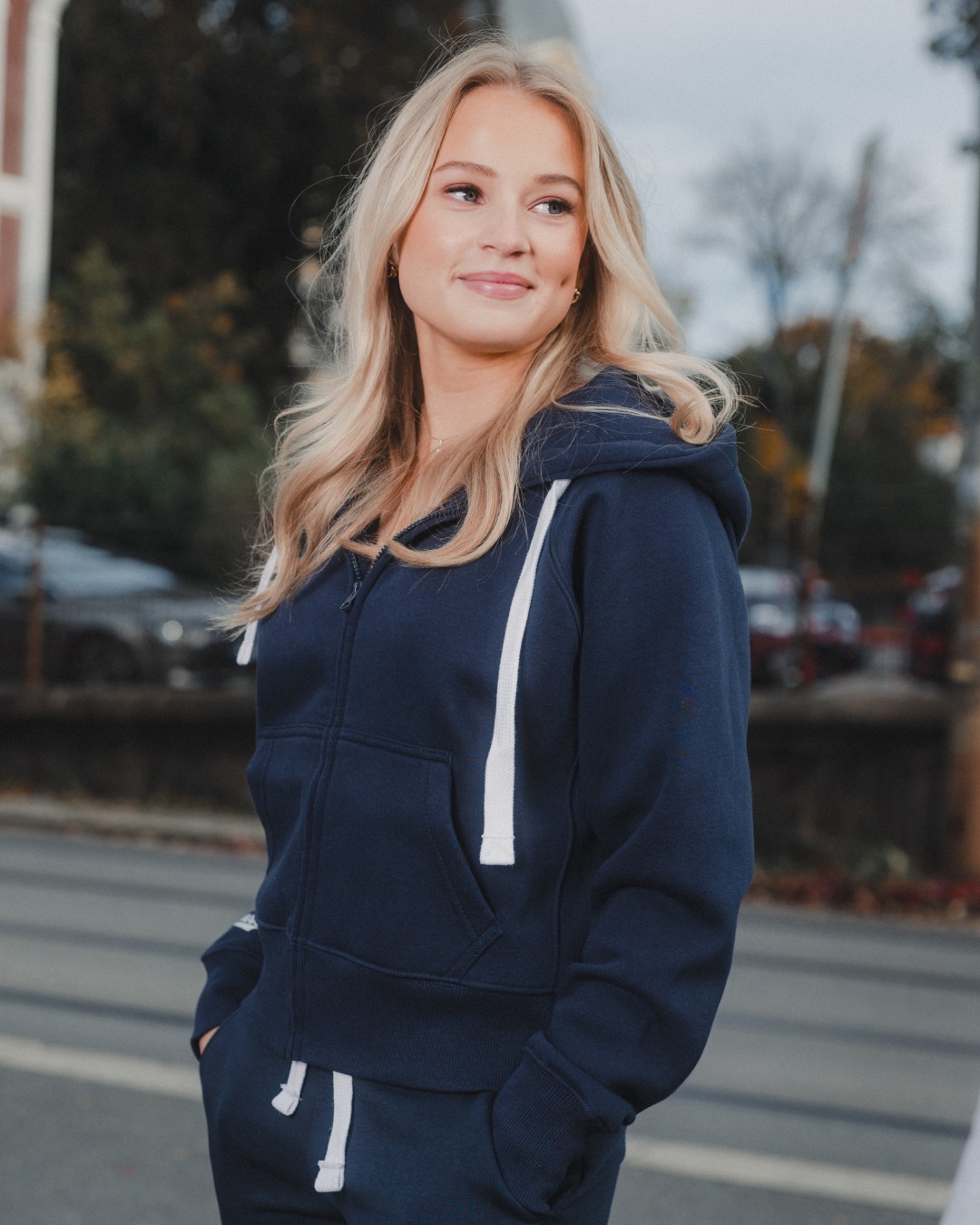 Blonde woman standing outside in an urban area wearing a dark blue zip hoodie and a dark blue sweatpant