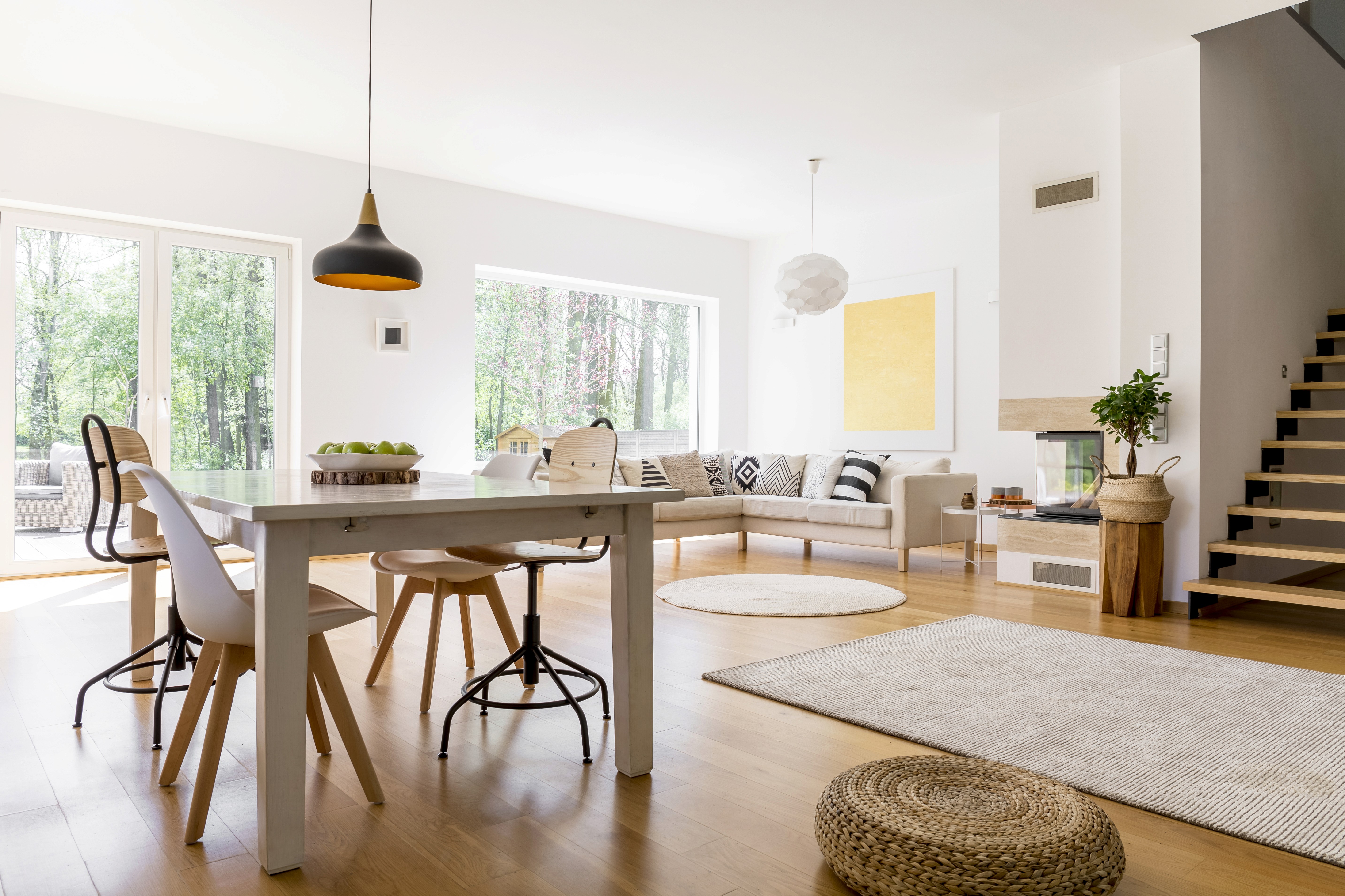 A person in a casual outfit is vacuuming a carpet in a bright, modern living room.