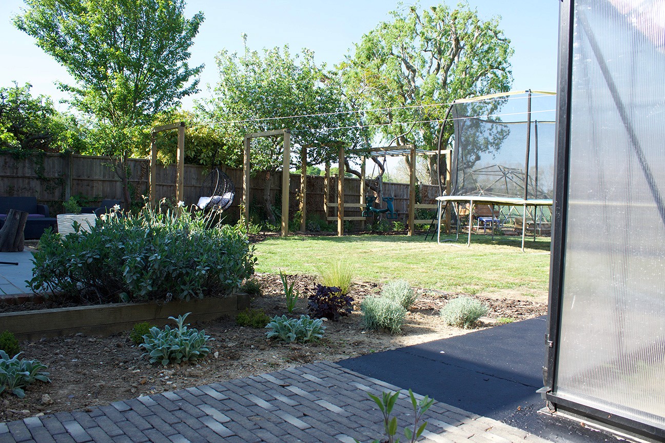 A sunny outdoor space with a grassy area, trees, and a path leading through a stone garden.
