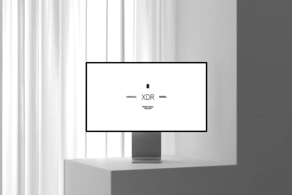 Minimalist computer monitor mockup with a sleek silver stand, displayed on a white pedestal near tall sheer curtains. The setting features soft natural lighting and clean lines.
