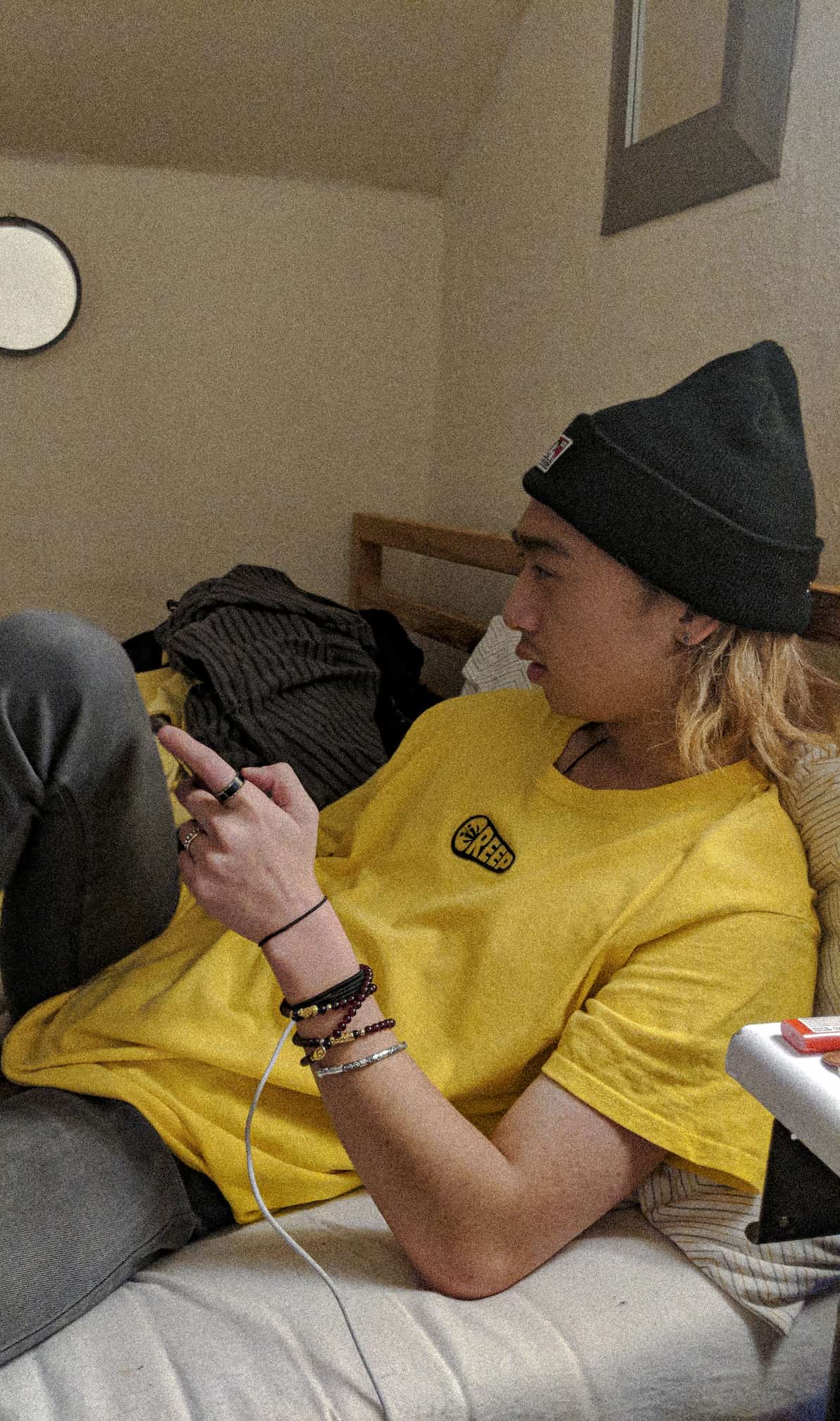 guy sat on bed in black beanie and wearing a yellow t-shirt with streetwear branding on t-shirt creep.