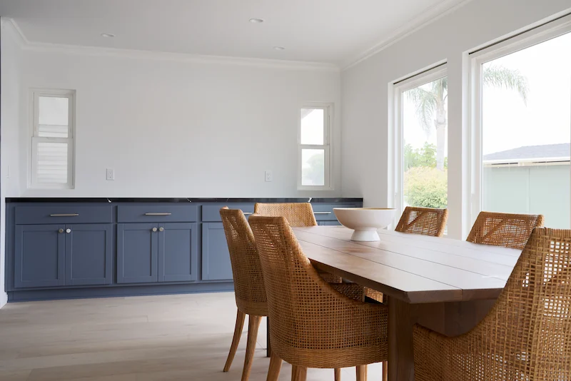 Dining space with a wooden table and chairs, blue cabinets, and open wall shelves. Photo by Todd Huge.