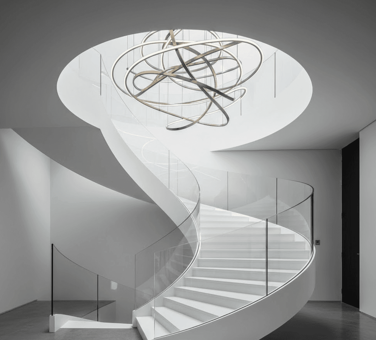 Sculptural ribbon-style staircase with continuous curved glass balustrade following organic flowing form. 