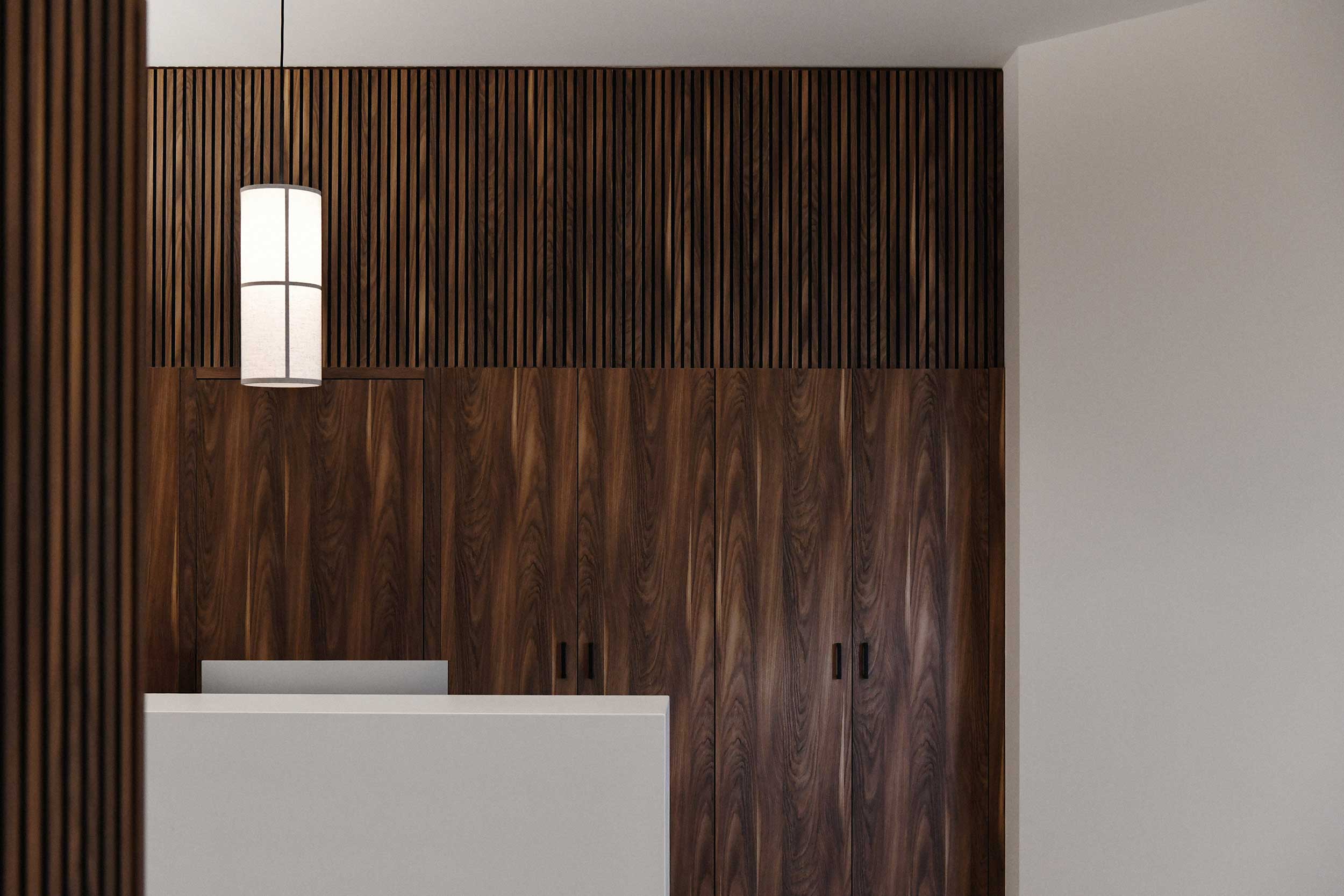 Empfangsbereich der Praxis SpinaMed mit weißer Theke, vertikaler Holzlamellenwand und hängender zylindrischer Leuchte.