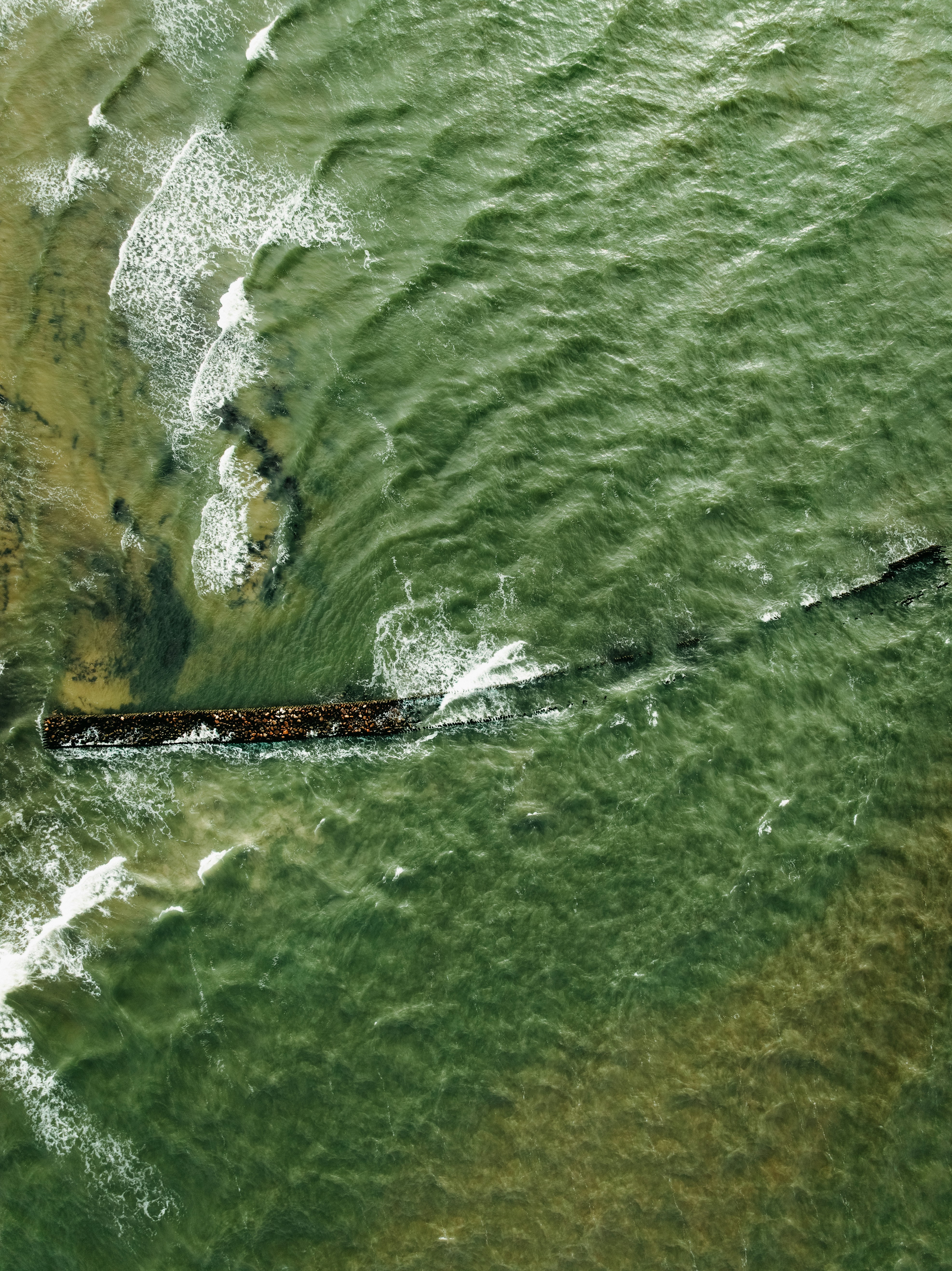 Waves crash over a submerged shipwreck at sea.
