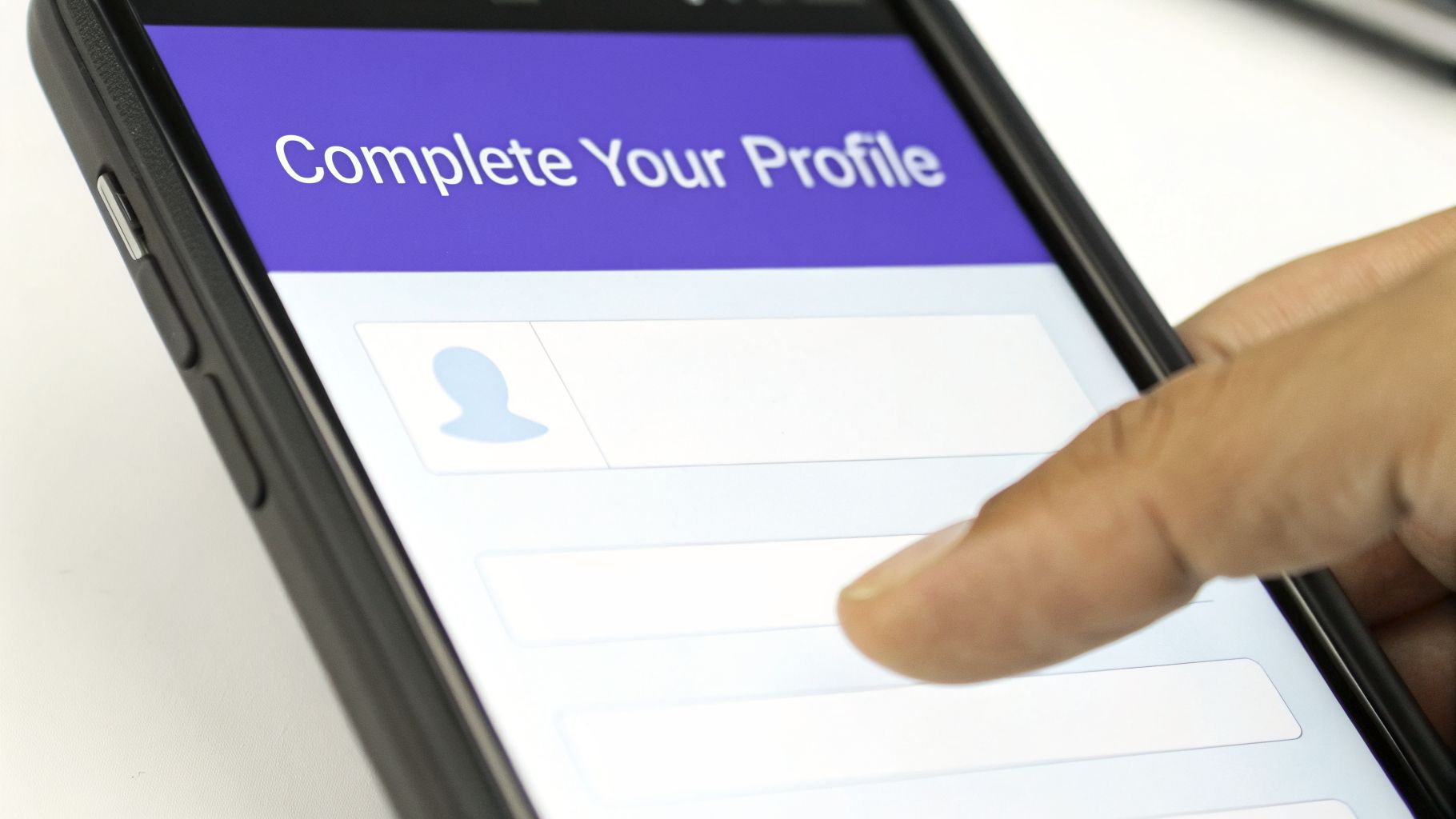 A hand interacts with a smartphone displaying a 'Complete Your Profile' screen with input fields.