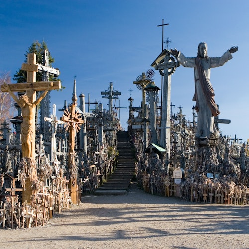 A hillside filled with numerous crosses, a large statue of Jesus with open arms, and a clear blue sky in the background.