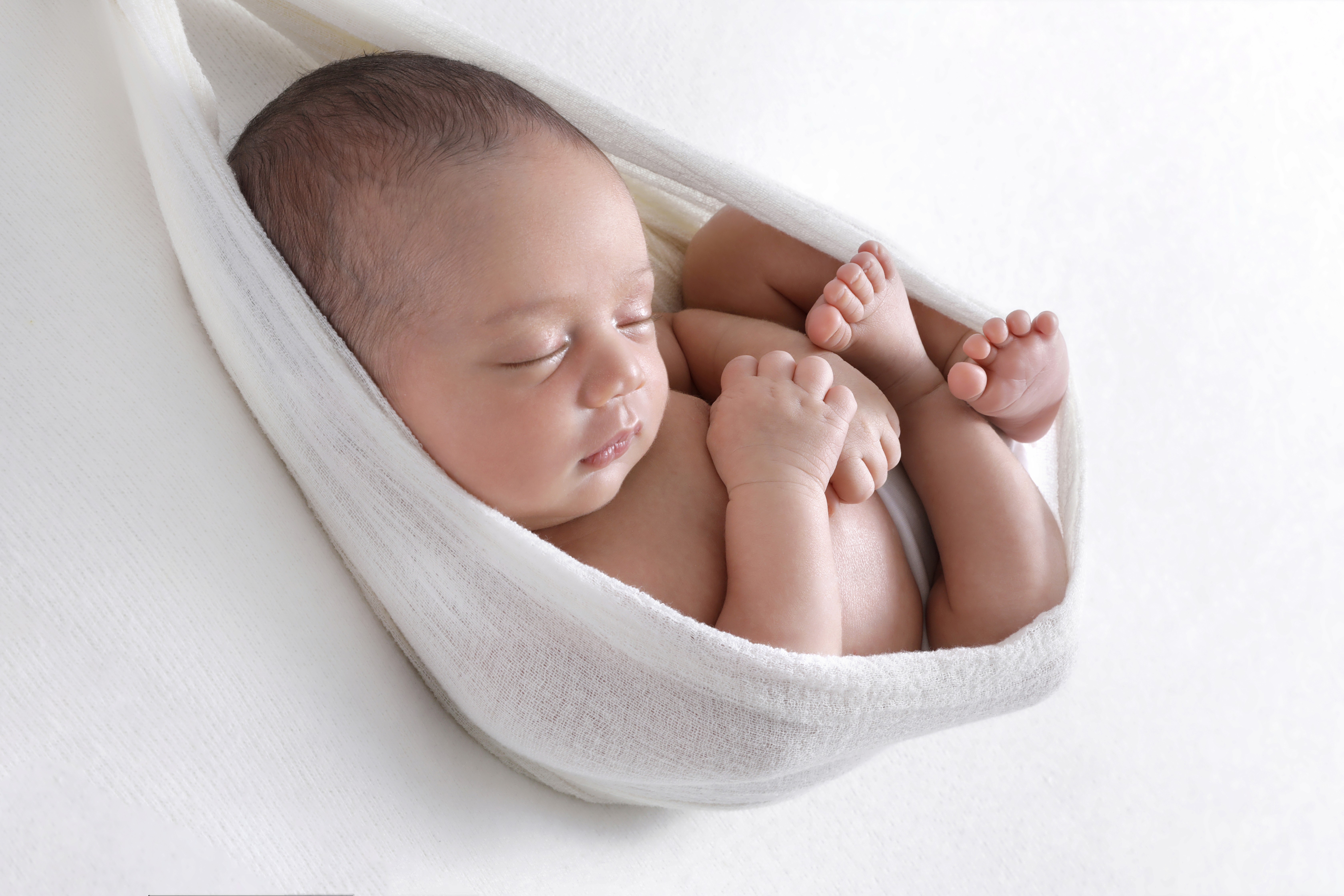 Newborn hospital photo capturing a sleeping baby peacefully swaddled in a soft white wrap, showcasing a tender and serene moment.