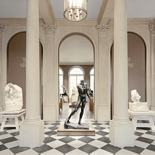 Muzejska galerija sa središnjim brončanim kipom, mramornim stupovima i nekoliko kamenih skulptura na postoljima, pod visećim fenjerom.