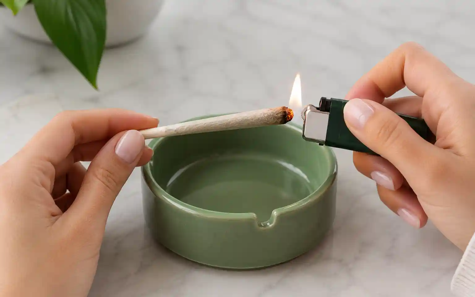 Person lighting a pre-roll with a lighter over a green ceramic ashtray
