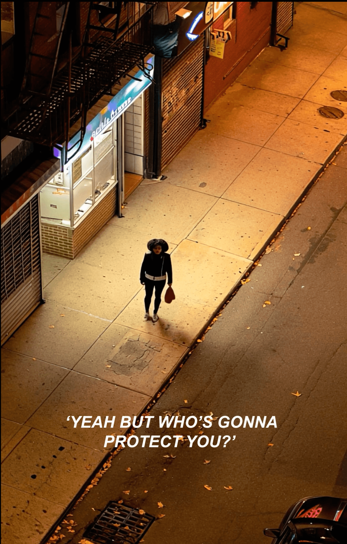 woman alone walking on a dark street with light from storefront