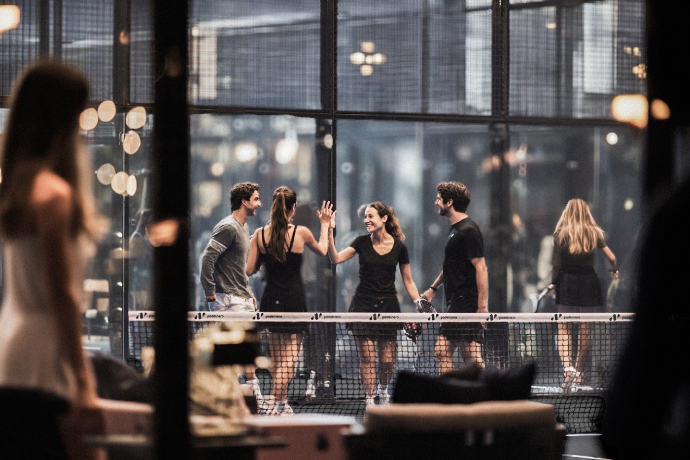 Vier Padelspieler feiern gemeinsam am Netz mit High-Fives – lebendige Stimmung und Gemeinschaftsgefühl auf dem stilvollen Padelnero Court.