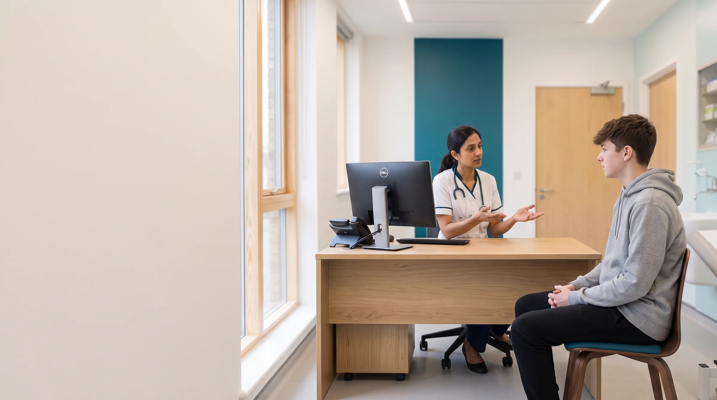 A GP explaining something to a teenage patient at the consulting desk